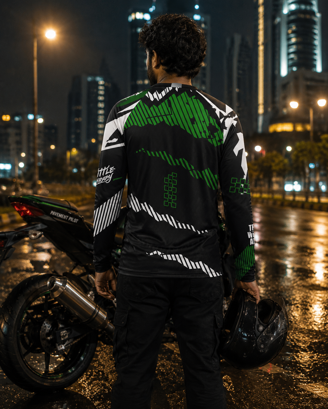 Person wearing a black and green jacket with a motorcycle on a city street at night.