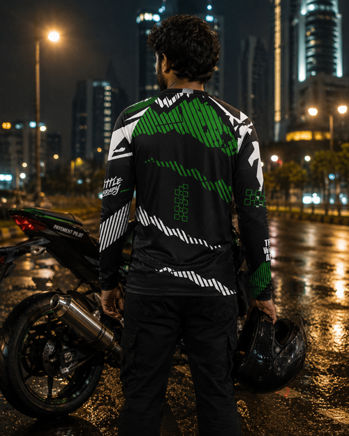 Person wearing a black and green jacket with a motorcycle on a city street at night.