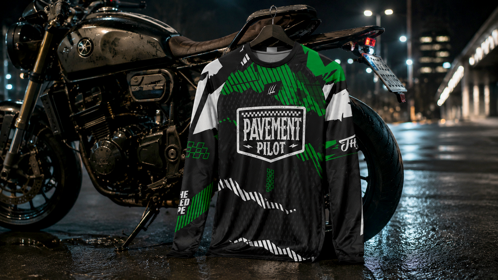 Motorcycle with a t-shirt featuring 'Pavement Pilot' branding on a wet street at night.