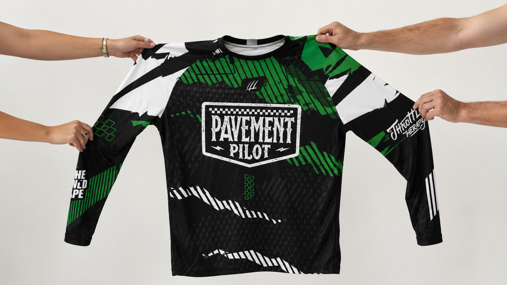 Green and black long-sleeve shirt with 'Pavement Pilot' logo held by four hands on a white background