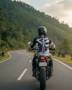 Person riding a motorcycle on a winding road with greenery and mountains in the background
