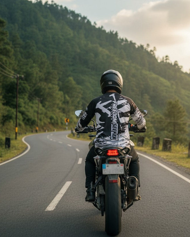 Person riding a motorcycle on a winding road with greenery and mountains in the background
