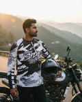 Man standing next to a motorcycle on a scenic road with mountains in the background