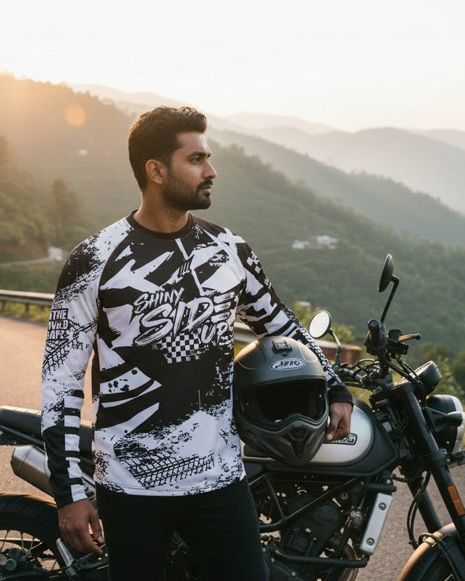 Man standing next to a motorcycle on a scenic road with mountains in the background