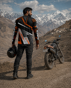 Man in motorcycle gear standing next to a dirt bike with mountains in the background