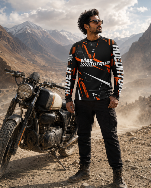 Man in a black and orange 'Max Torque' jacket standing next to a motorcycle in a mountainous landscape.